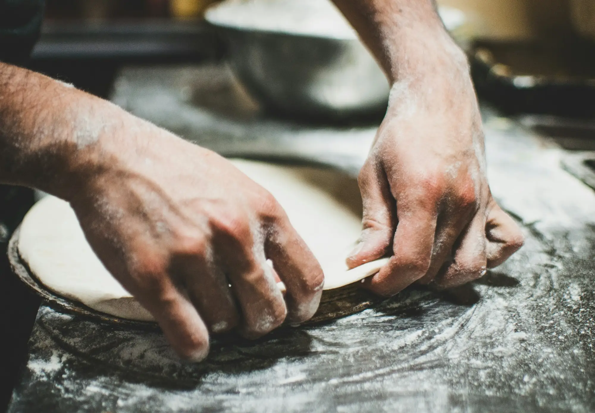 Mani che stendono un panetto di impasto sul banco
